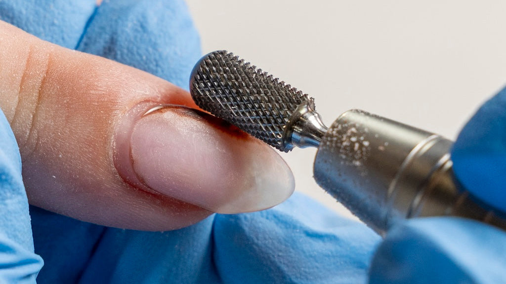 Close-up of a nail drill bit being held by a person wearing blue gloves.