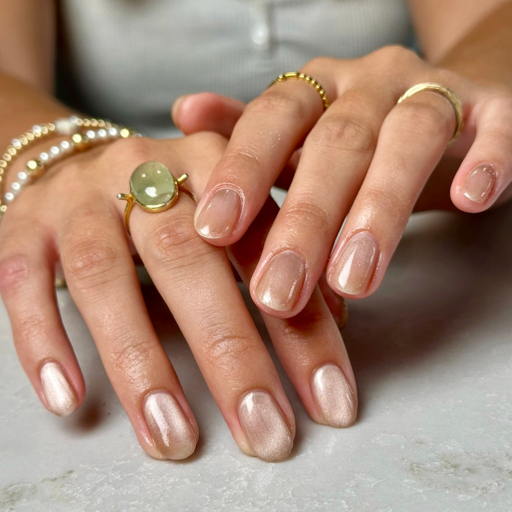 Close-up of hands with polished nails and gold rings on a neutral background