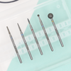 A set of five diamond nail drill bits of varying shapes and grits displayed alongside a clear bit case.